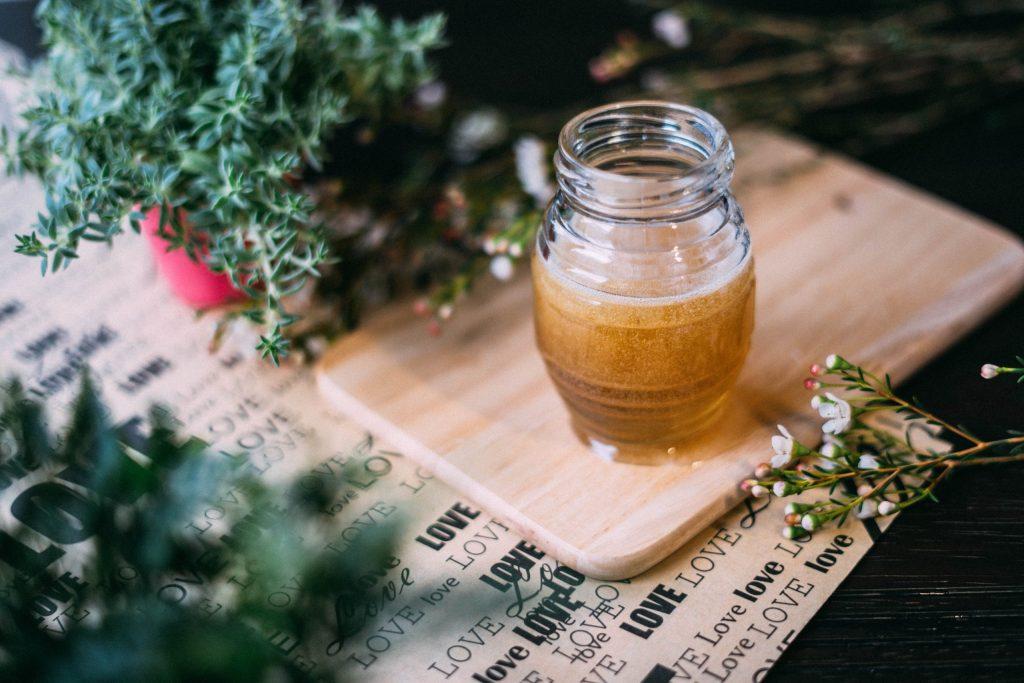 An open glass jar of vinegar on a placemat surrounded by sprigs of herbs.