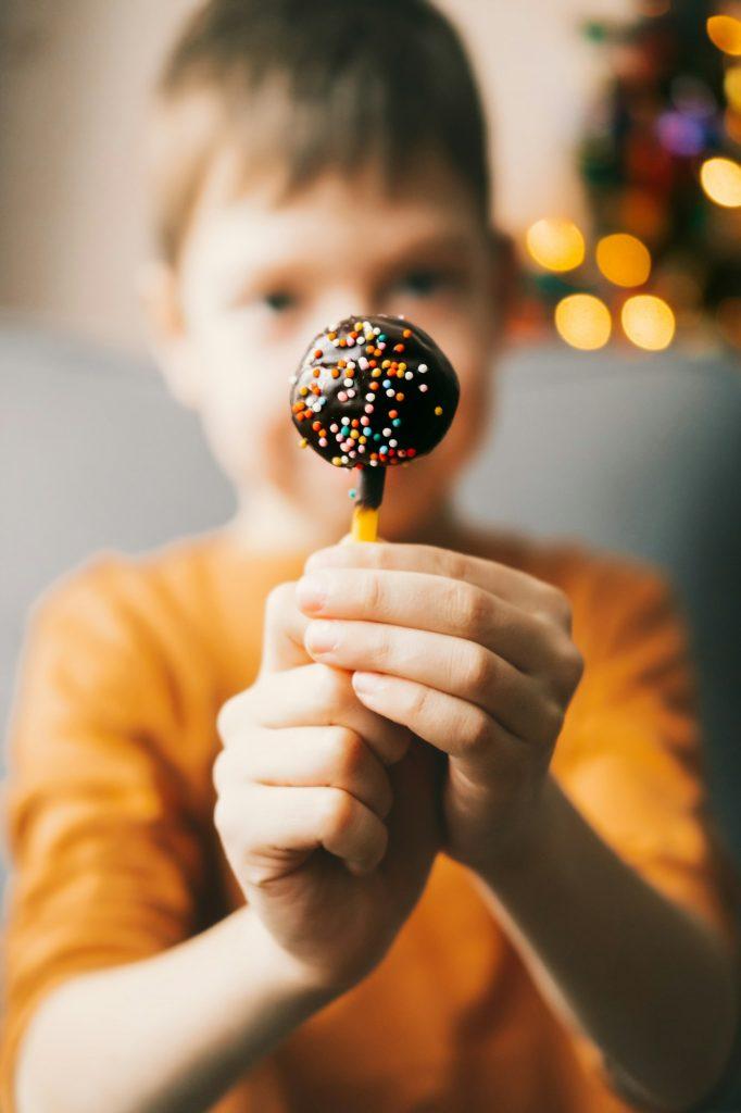 pops chocolate cake with multi-colored sprinkles, close-up, in the hands of a child.
