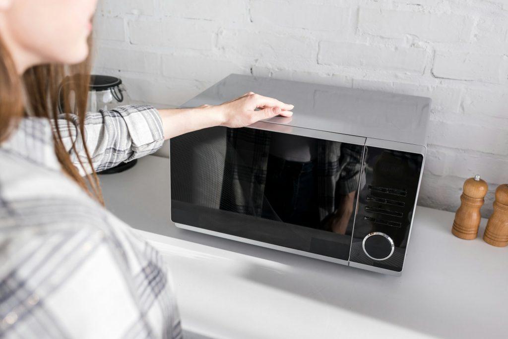 cropped view of woman looking at microwave in kitchen