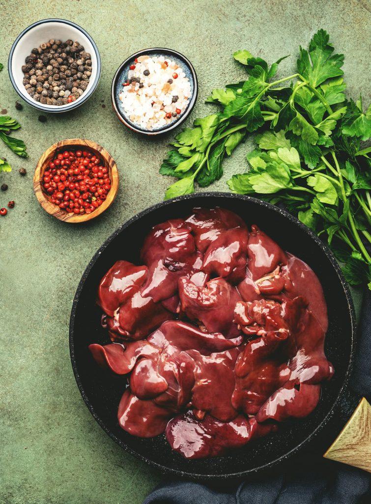 Fresh raw chicken liver in frying pan and ingredients for cooking on concrete green table