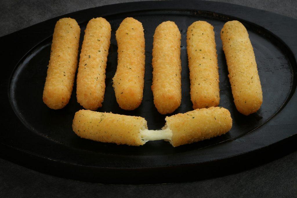 fried mozzarella sticks crispy on a black woden plate isolated on dark gray background