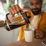 Young man pouring coffee from french press working indoors, home office concept