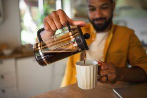 Young man pouring coffee from french press working indoors, home office concept